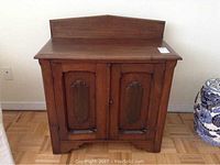 Front view of antique solid wood cupboard showing two paneled doors and raised back panel.