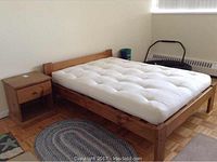 Overall view of wood double bed frame with white tufted futon mattress and wood night stand beside it.