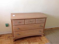Front view of light wood dresser showing 5 drawers with metal knobs and natural wood grain finish
