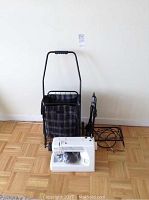 Photo showing two shopping cart buggies and a white Kenmore sewing machine arranged on wooden floor against white wall.