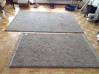 View of two beige shag area rugs placed on a wooden parquet floor, showing overall wear and dirt.