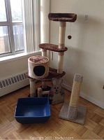 Photo showing the cat tower, scratching post, mouse cat toy and litter box together in room corner with parquet flooring and window.