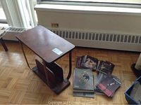Photo of the antique wooden side table with curved edges and magazine rack base, showing visible wear on the tabletop.