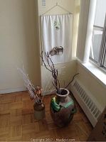 Photo showing textile wall hanging with rabbits, large ceramic pot with bird and branches, and smaller ceramic pot with white-painted branches.