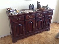Front view of Crawford Furniture wooden sideboard with four doors and three drawers, showing wear and several items on top not included in sale.