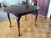 Full view of dark wood dining table without leaf extension, showing cabriole legs and wood floor background.