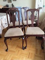 Four wooden dining chairs with upholstered seats arranged in a dining room area, showing the front and side angles.