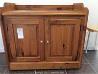 Front view of wooden cabinet with double doors and brass knobs, showing natural wood grain and bottom drawer