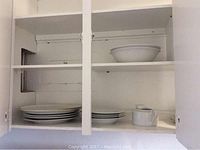 Kitchen cabinet with stacked white plates and a white ceramic creamer.