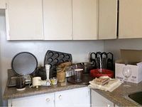 Full view of kitchen counter with various kitchen items including pans, baking sheets, wine glasses, chopper and wooden mortar and pestle.