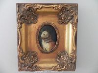 Oval cat portrait in small ornate gold frame with decorative corners.