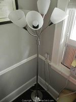 Photo of metal floor lamp with five white frosted glass shades, adjustable arms, standing in corner by window.