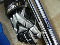 Close-up image of Brine brand lacrosse gloves and lacrosse sticks with white and blue shafts