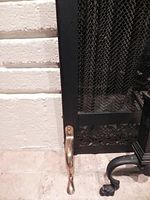 Close-up of bottom left corner showing brass foot and black metal frame with mesh screen, highlighting condition with minor pitting and scratches.