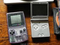 Photo of two handheld Game Boys: purple transparent Game Boy Color and silver Game Boy Advance SP laid on wood floor.
