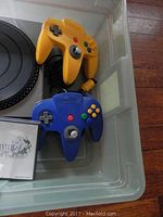 Photo of yellow and blue Nintendo 64 controllers next to DJ Hero turntable and game cases