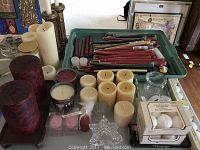 Overview of assortment of candles and candle holders spread on a table including pillar, taper, votive candles, and assorted holders.