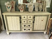 Front view of shabby chic buffet showing crackle finish paint, six small center drawers, two side doors, black wrought iron pulls, and jewelry displayed on top.