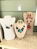 Overview of three necklaces and two pairs of earrings displayed on busts