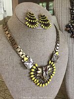 Gold tone necklace with large clear and yellow glass insets displayed on necklace bust, with matching earrings hanging above.