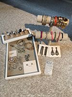 Wide view showing rings on white ring display, bracelets on two horizontal T-bar displays, and earrings in front on cards and surface.