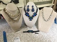 All five jewelry pieces displayed on three bust stands: two gold-tone necklaces, one floral iron-tone necklace, matching earrings and bracelet below