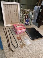 Overview of necklaces displayed on white stand, earrings, picture frame, decorated box and iPad case on carpeted floor.