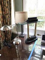 Photo showing all three lamps on a table near a window including the brushed metal gooseneck lamp, lamp with cloth shade, and LED halogen lamp with glass shelf and dimmer.