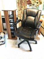 Photo showing front view of black faux leather office swivel chair and wooden CD tower with multiple CD slots.