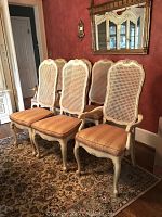 Photo showing four of the six Thomasville caned back dining chairs with upholstered seats positioned side by side on a rug with a mirror and wall sconces in the background.