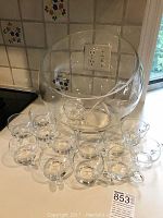Wide shot showing large clear glass punch bowl and twelve clear punch cups arranged in front of it.