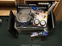 Box with various electronic accessories including Ergonomic Lighted Lapdesk, Coby Compact Disc Player, wireless LED lights, a princess phone, and other items.