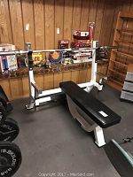 Overall setup showing white steel bench frame with black pad, barbell loaded and plates on floor