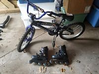 Blue and black Rhino Blade On The Edge bike standing on floor, with a pair of black Roller Derby inline skates placed in front of it.