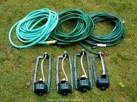 Three coiled garden hoses in light aqua blue, dark green, and teal colors, placed on grass, with four Melnor oscillating sprinklers in front of them.