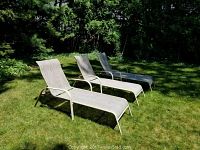 Three outdoor chaise lounge chairs on grass with tubular metal frames showing minor rust spots