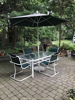 Outdoor glass dining table with four matching chairs and green umbrella set on patio.