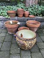 Full lot showing large Asian style ceramic planter, multiple clay pots stacked and spread out, and black cast iron urns on stone patio with stone steps and ivy in background.
