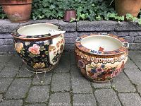 Two large round ceramic planters side by side on outdoor stone pavement with ivy in background.