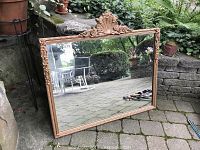Full view of large vintage wall mirror with painted wooden frame and applied floral and shell carvings, positioned outdoors on stone tiles.