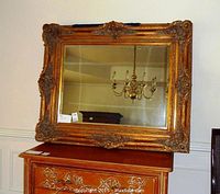 Full view of the large rectangular mirror on wood dresser showing gold ornate frame with carved details and antique style.