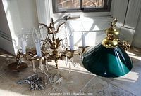 Photo showing the antique chandelier with six candle-style bulbs and crystal prisms along with the green glass pool table lamp with brass fittings lying on tiled floor near a window.
