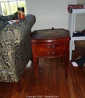 Front side view of occasional table showing single drawer and leather inlay top next to patterned sofa.