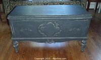 Black distressed finish wood chest with decorative carved drawer front, photographed from front angle.