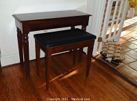 Console table with mahogany finish and upholstered leather bench in front, positioned on a wooden floor near a door holding a decorative ship model.