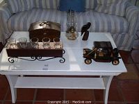 Photo showing all items on white table in front of couch, including votive candle holder, kerosene lamp, wooden bird, wooden antique car, and tray.