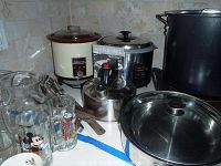 Overview of lot on kitchen counter including large stockpot, pans, crockpot, steamer, kettle, grill tools, and drinkware.