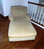 Front view of honey colored chaise lounge with rounded bolstered arms and cushioned seat on wooden floor.