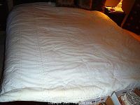 White king comforter with lace edging spread on bed, with side view showing condition.