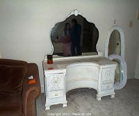Front view of antique white painted vanity with attached scalloped mirror, visible distressed paint and four drawers.